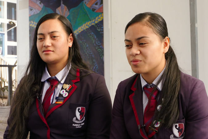 Two students in school uniform sitting outside.