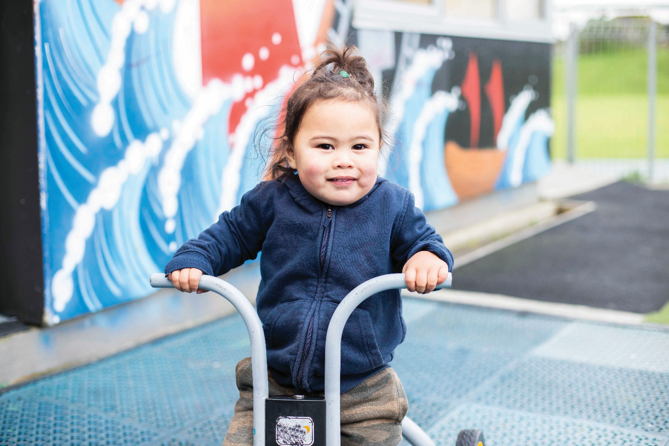 A tamariki on a tricycle smiling at the camera.