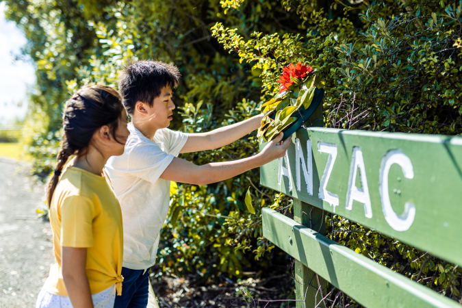 A young boy and girl paying their respects to the Anzacs by laying down a poppy on a memorial sign.