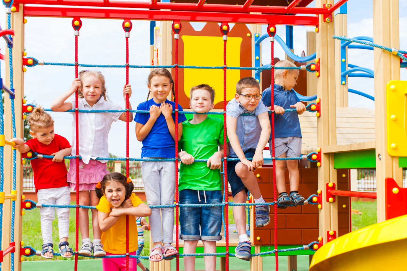 Children smiling at the camera as they play on the playground.