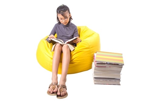 A child is sitting on a bean bag, reading a book.