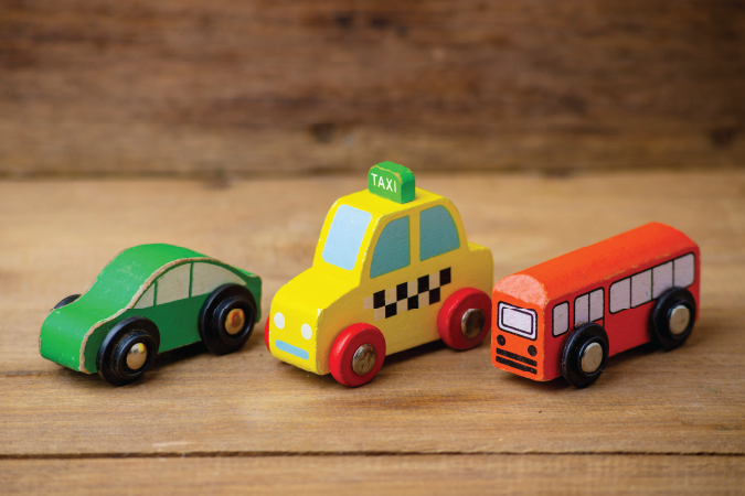 A green car, a yellow taxi, and a red bus on a wooden surface.