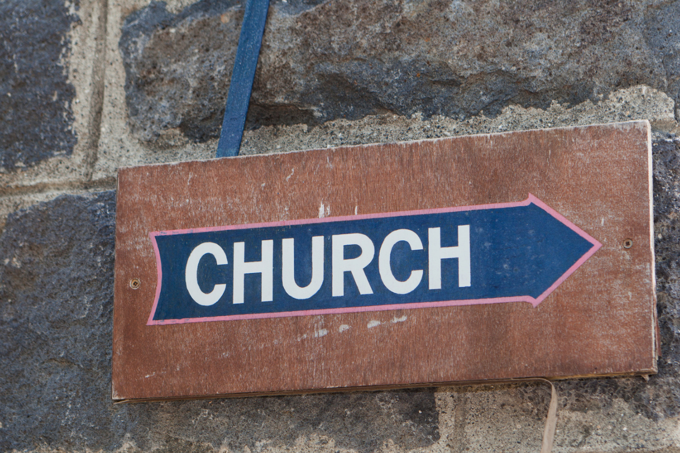 The word church painted inside an arrow pointing right, on a wooden sign.