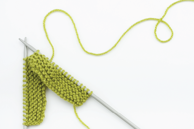 Knitting needles stitching a green pattern.