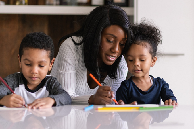 An adult helps two children with their homework.