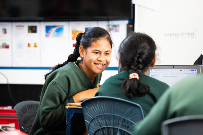 Two students are talking together while sitting at a table.