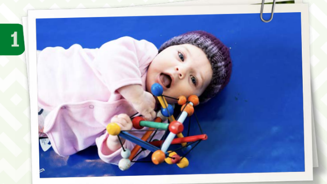 Part of the front page of the Play-ideas-for-learning information card. It contains a picture A baby lying on their back holding a wooden toy. There is a number ‘1’ next to the picture of the baby.