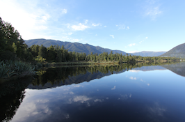 Mountains and trees are reflected in the calm water.