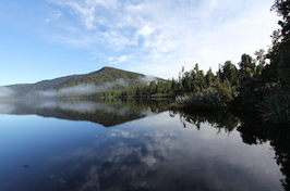 A mountain is reflected in a body of water. There is a forest along the one side of the water.