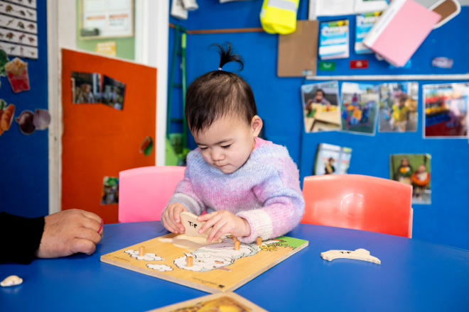 A young girl placing the pieces together of a wooden shapes puzzle.