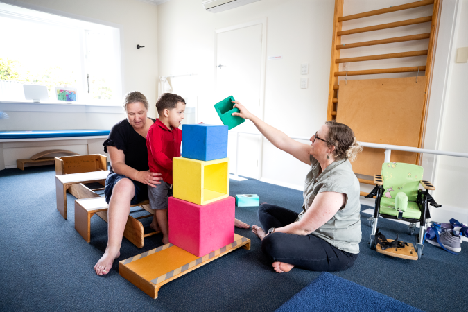 Two kaiako and a child playing with large coloured blocks.