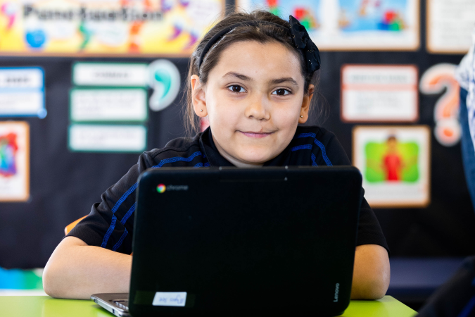 A student in a classroom, sitting at a table with a device.