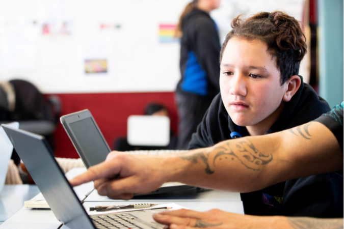 A student observing an adult pointing to the screen of a device.