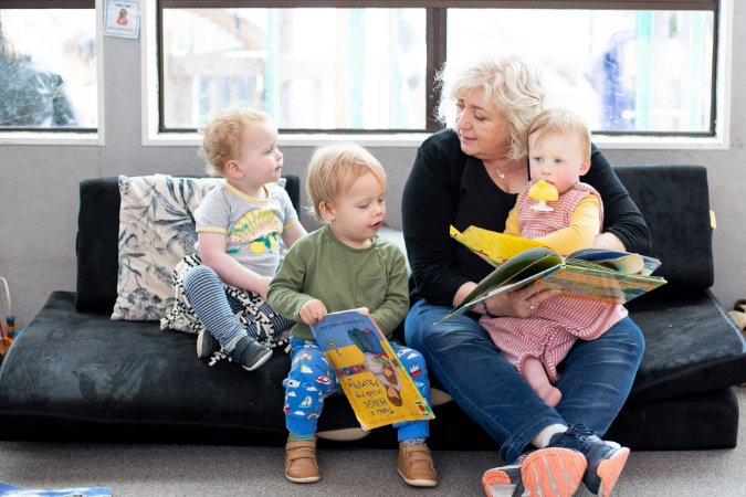 A kaiako and children on a couch playing and interacting with picture books.