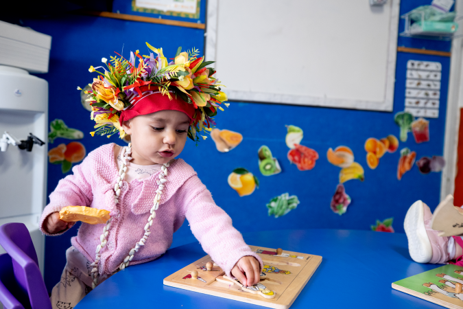 Child playing inside at a table with a wooden shapes puzzle.