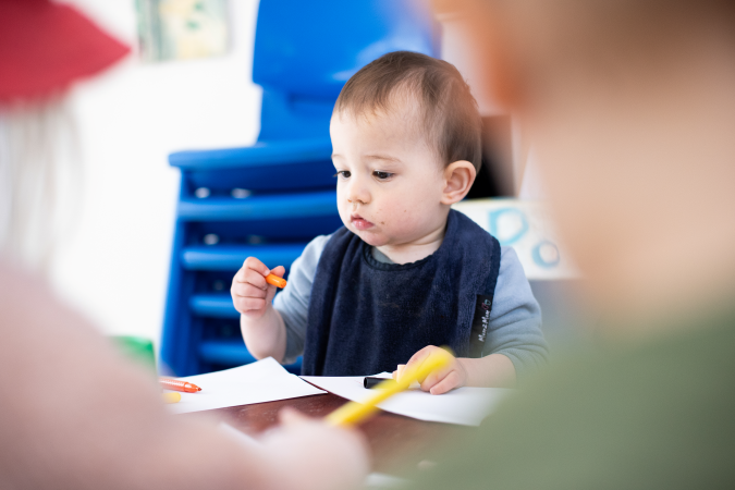 A young child at a table colouring paper with crayons.