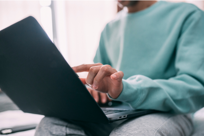 A person with a device in their lap, pointing to the screen.