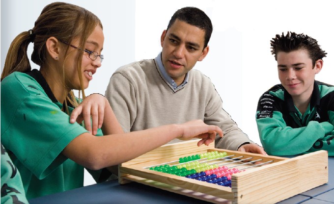 Teacher and two students sit together in the classroom counting numbers on an abacus.