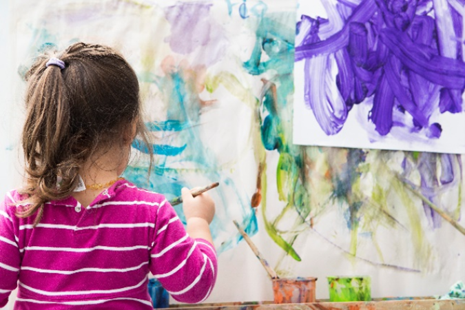 A young young girl paints at an easel.