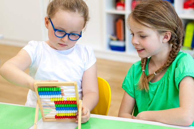 Two girls sitting at a table using an abacus.