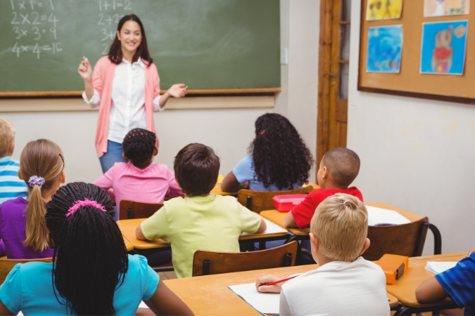 Students sitting at their desks in the classroom listening to their teacher.