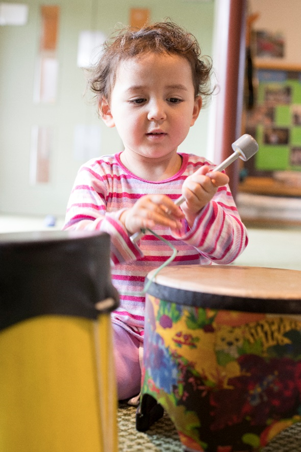 Young child sitting on the floor playing with a drum.