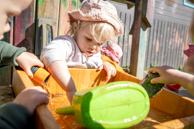 A young child with other children playing outside around a water tub with toys.