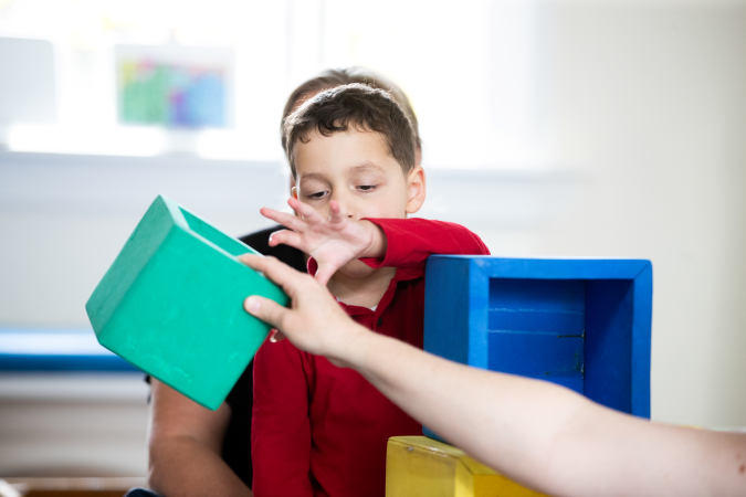 A kaiako and child playing with large coloured blocks.