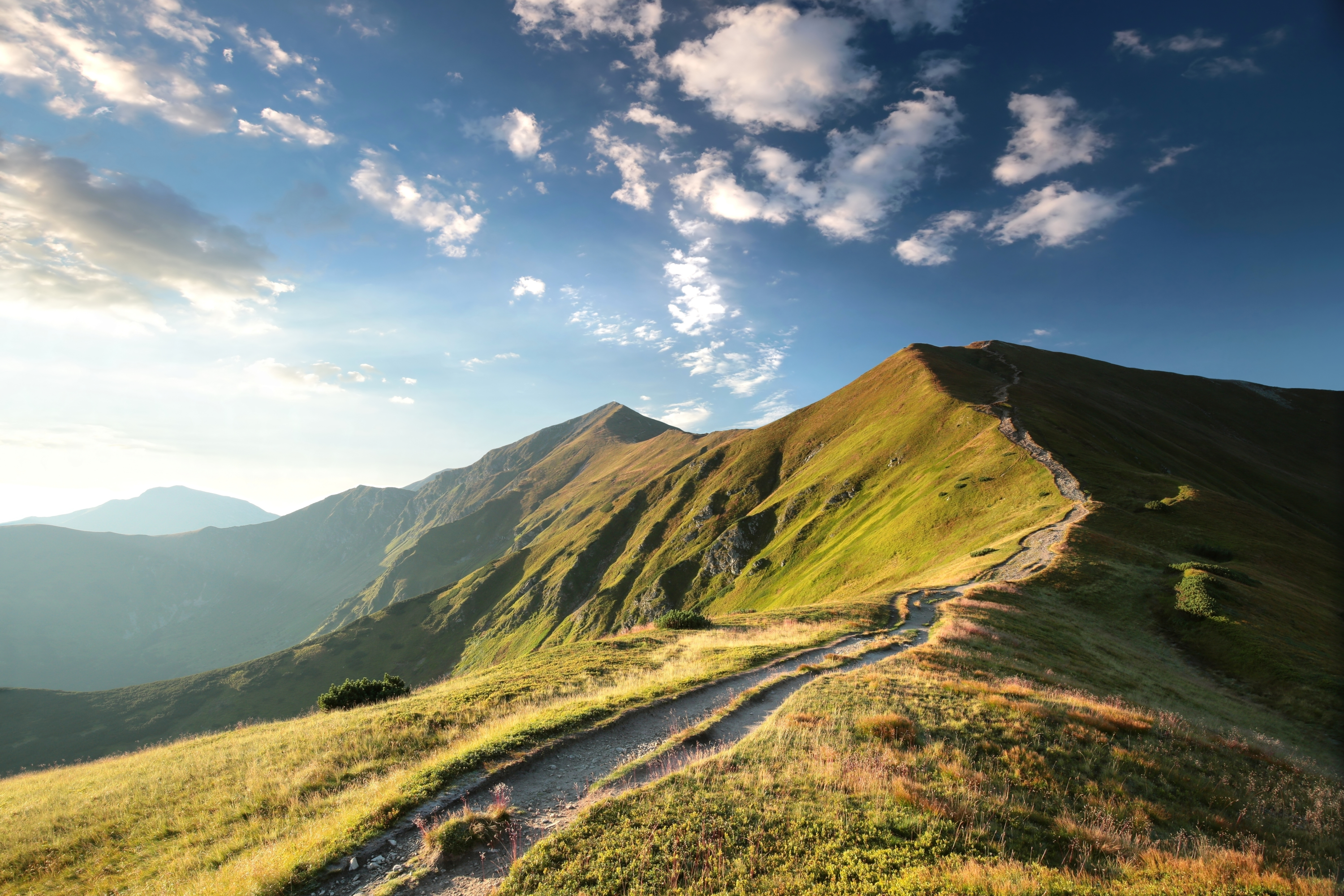 Bright sun shining over a range of grass covered mountains with a blue sky. 