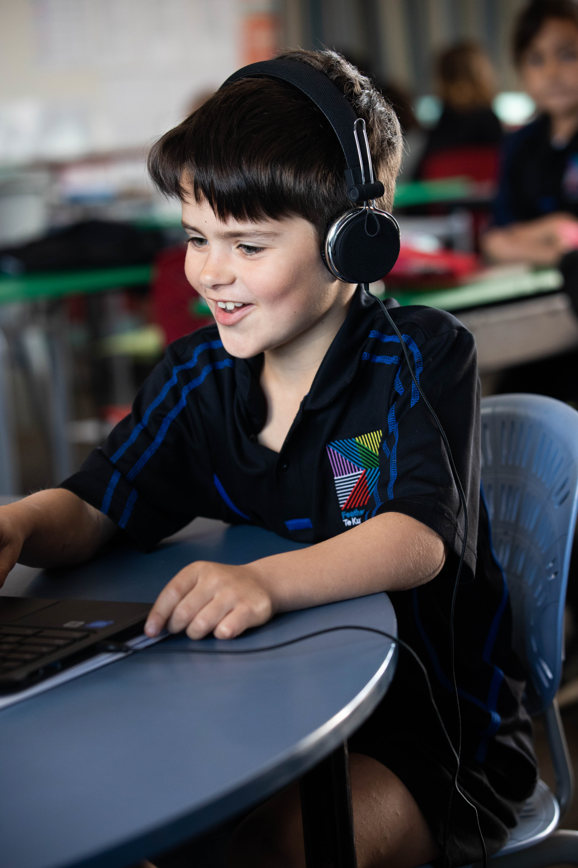 A young boy in his school uniform, wearing a headset, looking at a laptop. 