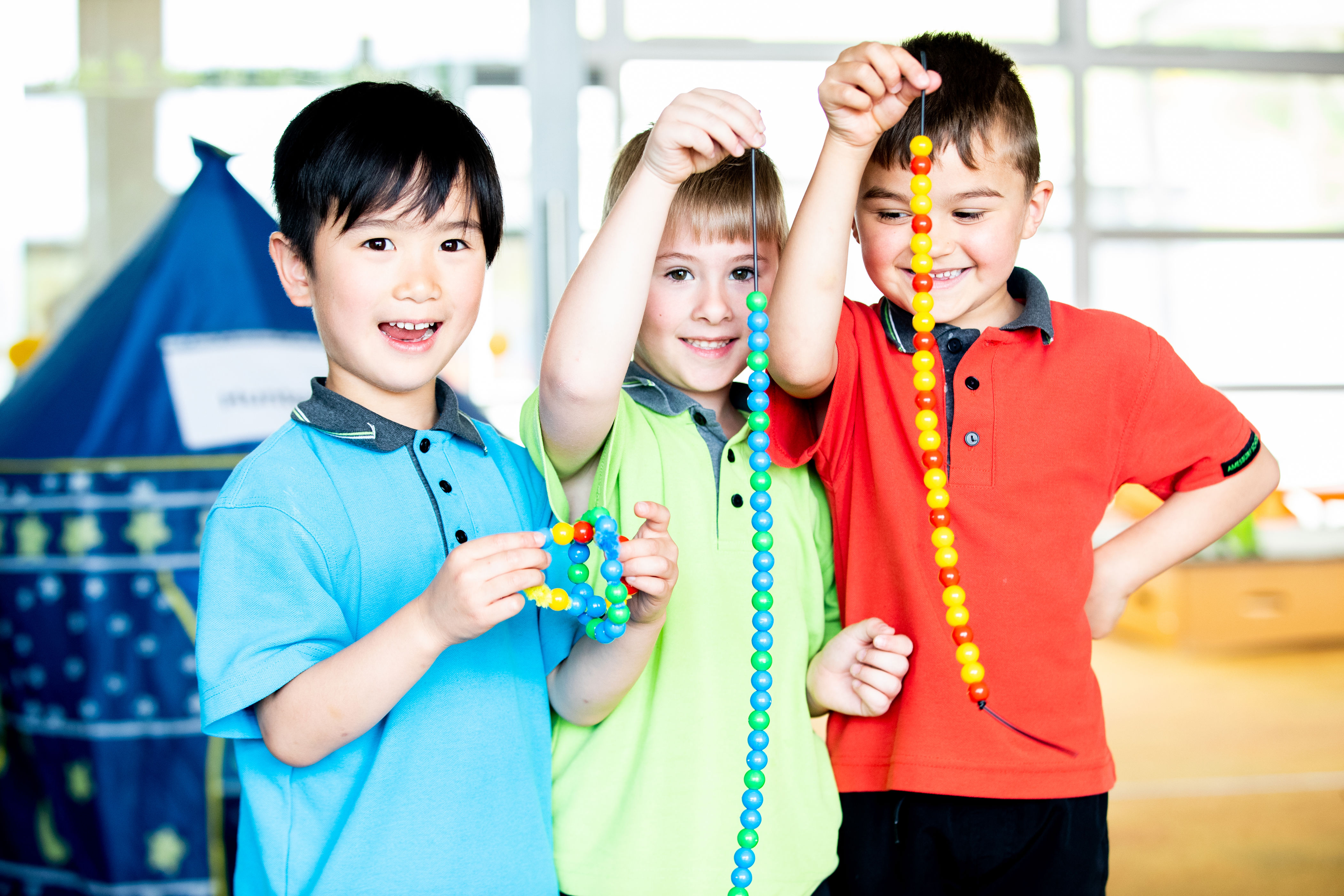 three kids holding a string of beads, looking pretty happy