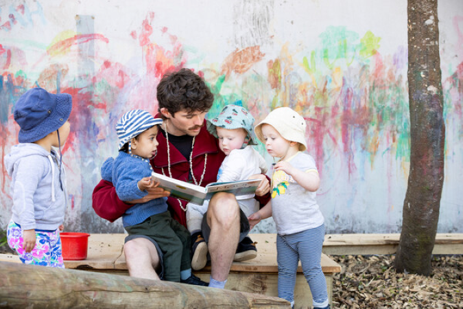 Adult and small group of children reading a book outside