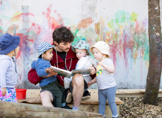 Adult and small group of children reading a book outside