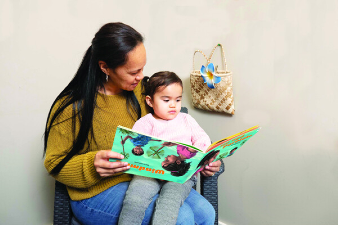 Child sitting on adult's knee reading a book