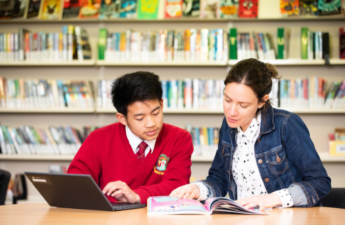 kid and teacher looking at a book together at a desk