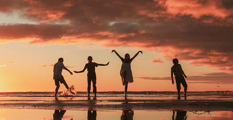 Four children playing on the beach in very shallow water at sunset