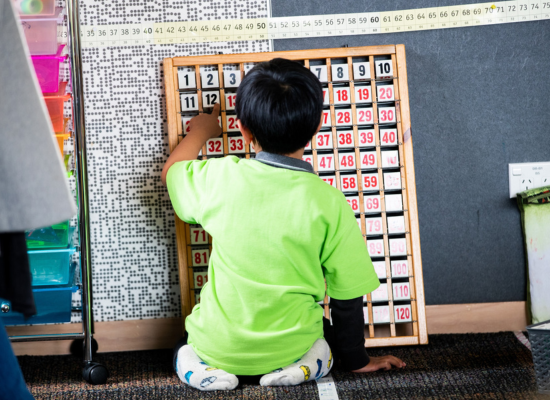 A student sitting on the floor, engaged in an activity with a 0–120 flip board.