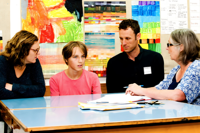 Three teachers sitting at a desk with a student.