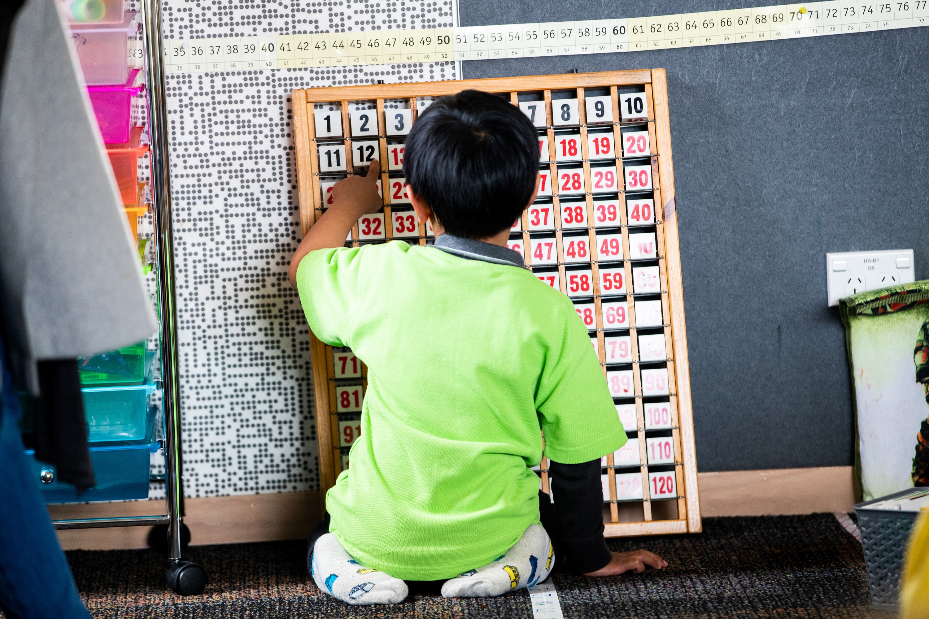A student sitting on the floor, engaged in an activity with a 0–120 flip board.