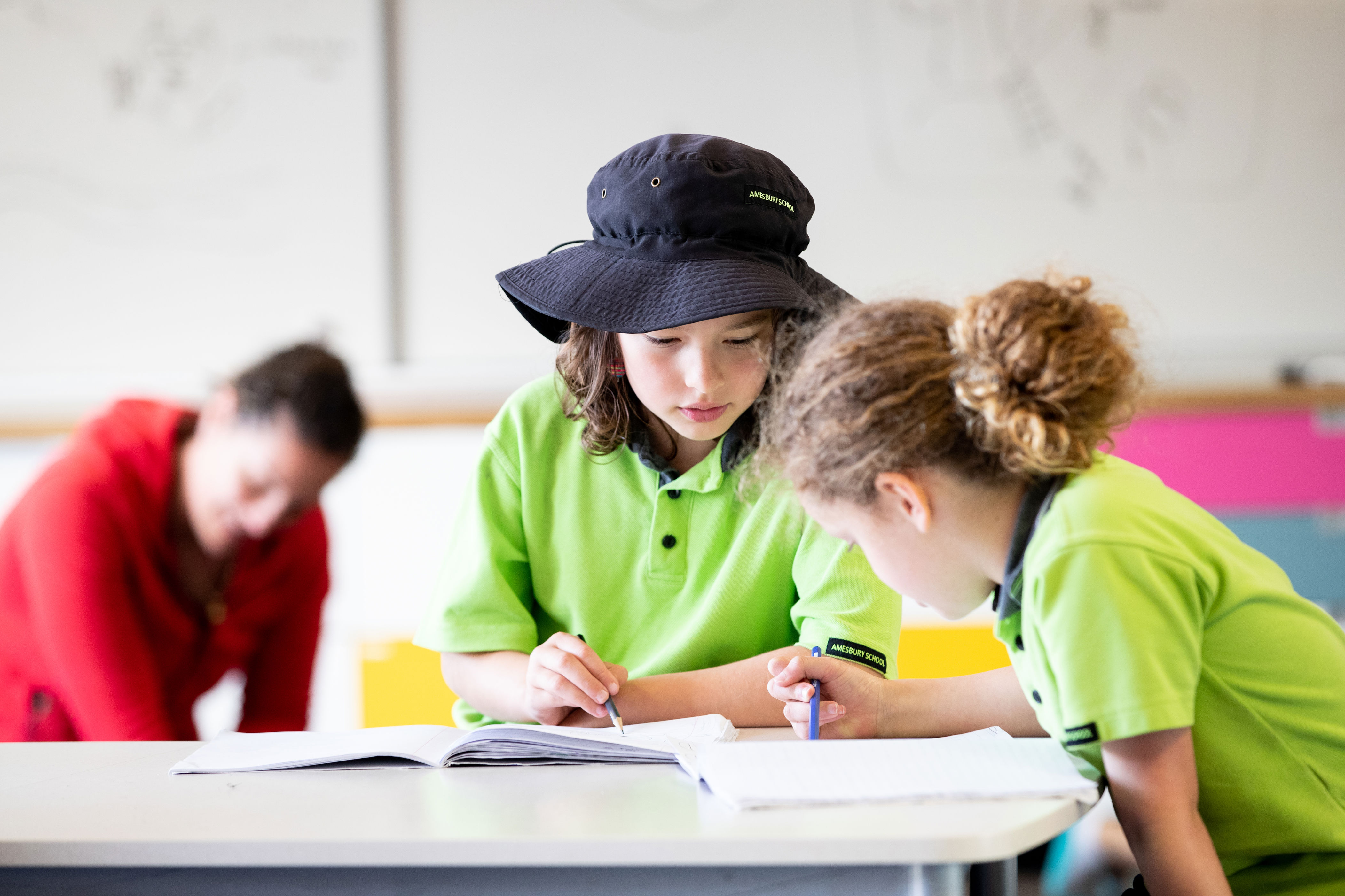 Two primary school aged students work together on a task, while they collaborate over an open notebook.