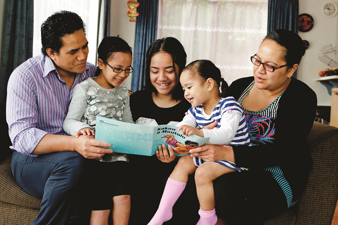 Family sit on the couch reading a picture book together. 